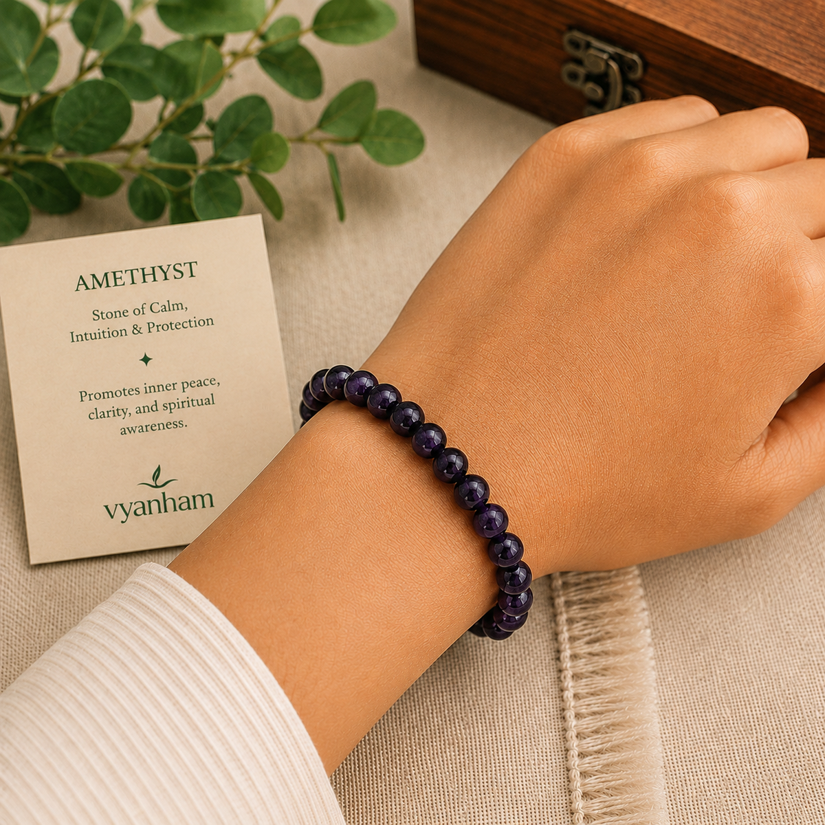 Hand wearing an amethyst bracelet with a card explaining the stone's properties, on a neutral background.