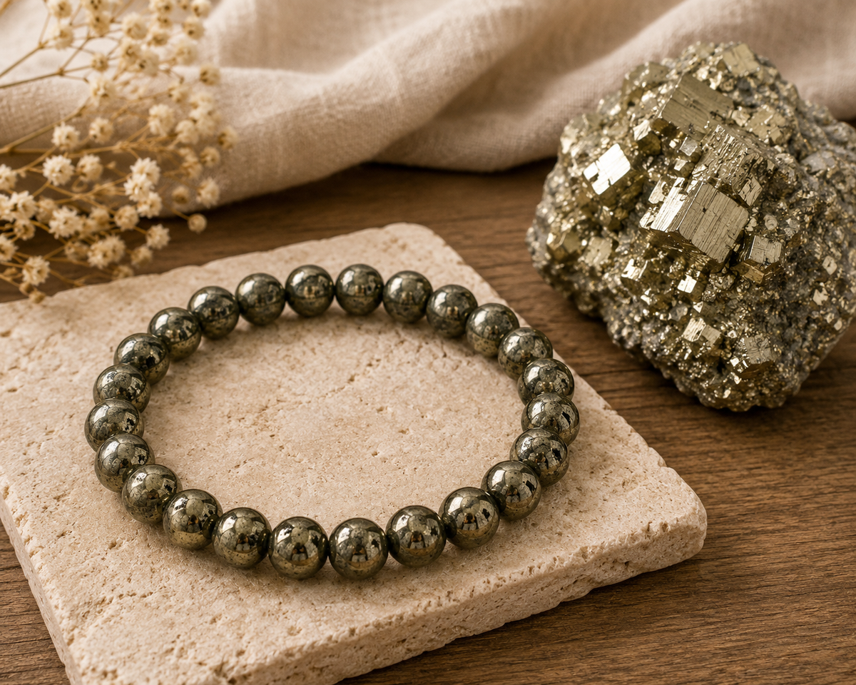 Pyrite bracelet resting on a stone coaster beside a raw pyrite crystal on linen and wood
