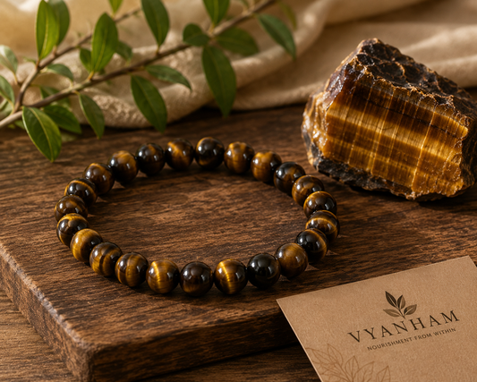 Tiger eye bracelet resting on a stone coaster beside a raw tiger eye crystal on linen and wood